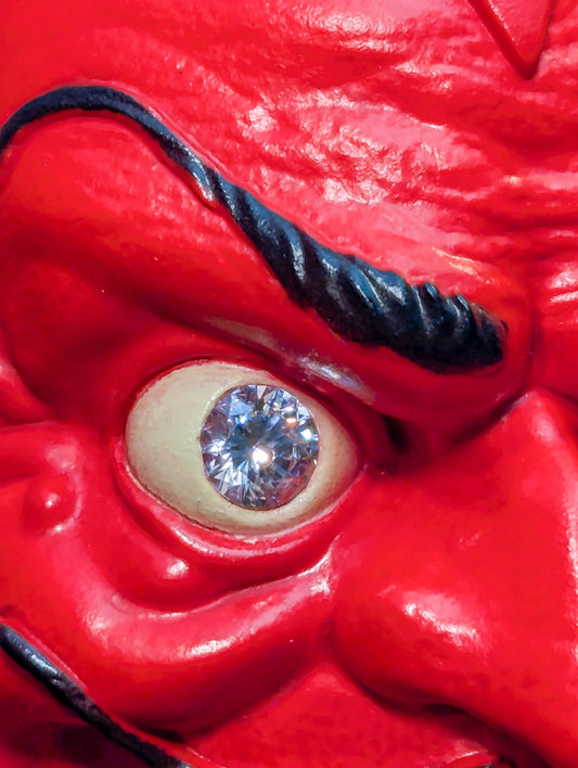 A closeup of a red devil sculpture’s sparkly gem eye