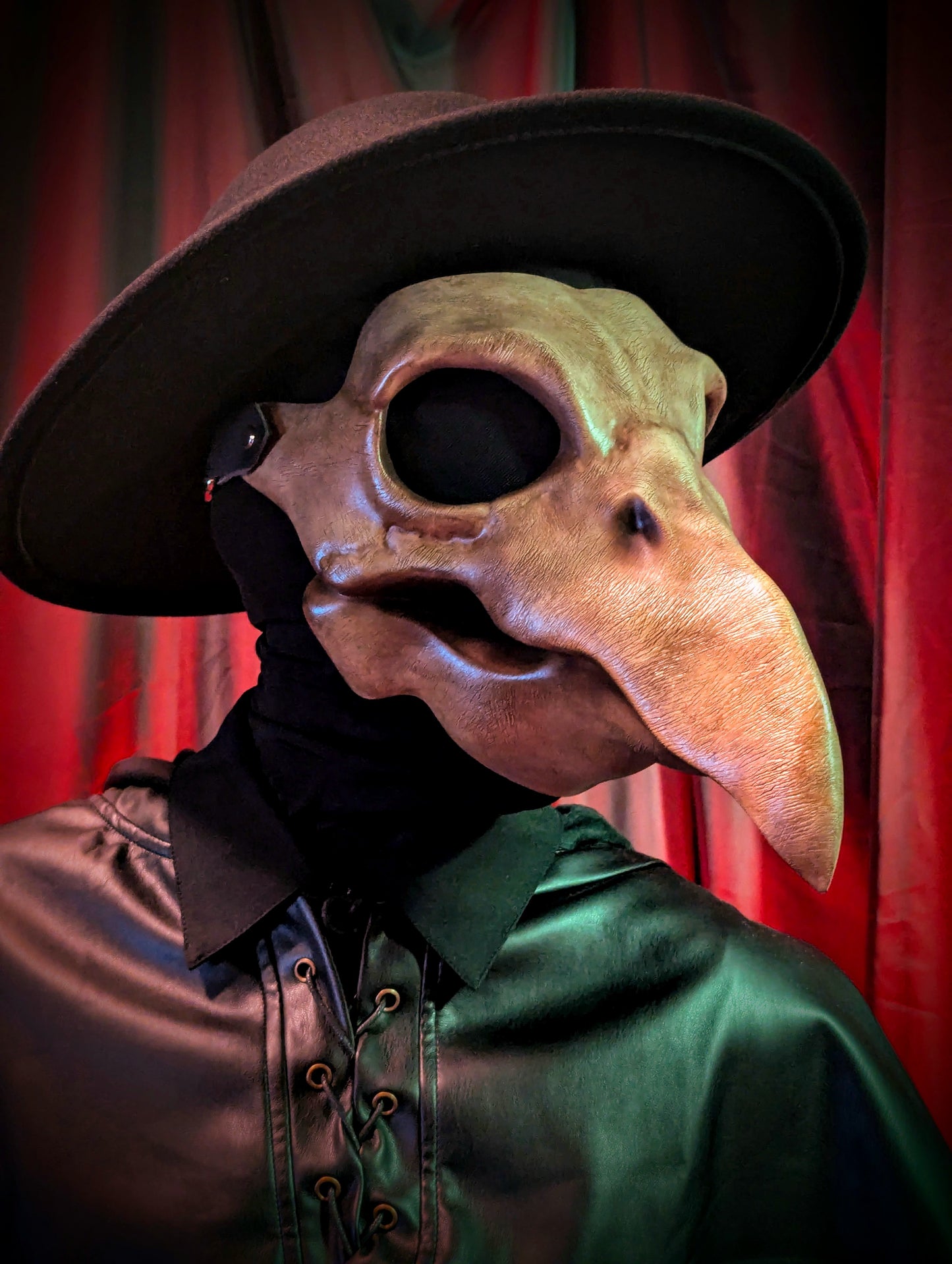 Person wearing a plague doctor mask and outfit against a red curtain background