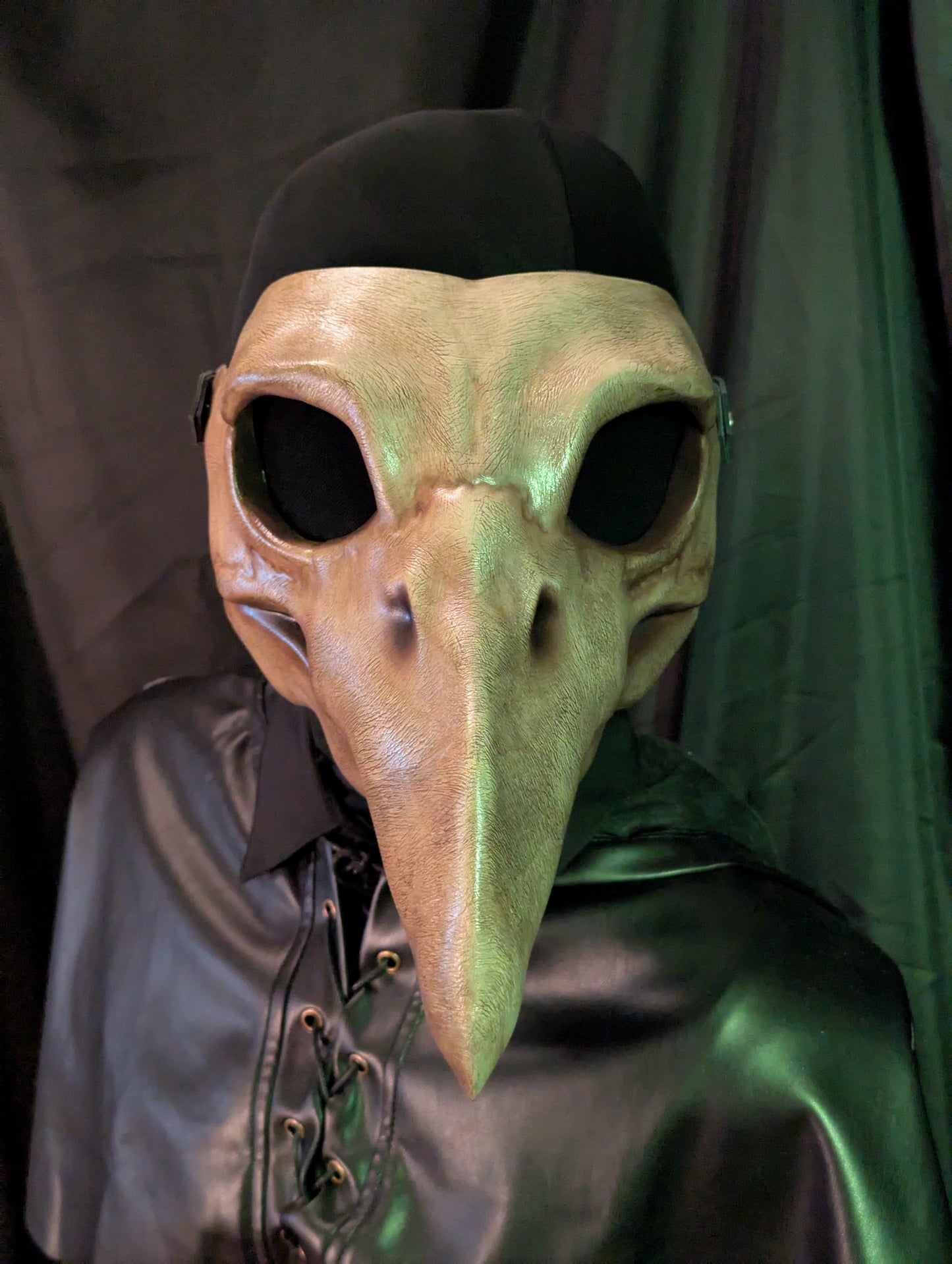 Person wearing a bird-like mask with a long beak against a dark background