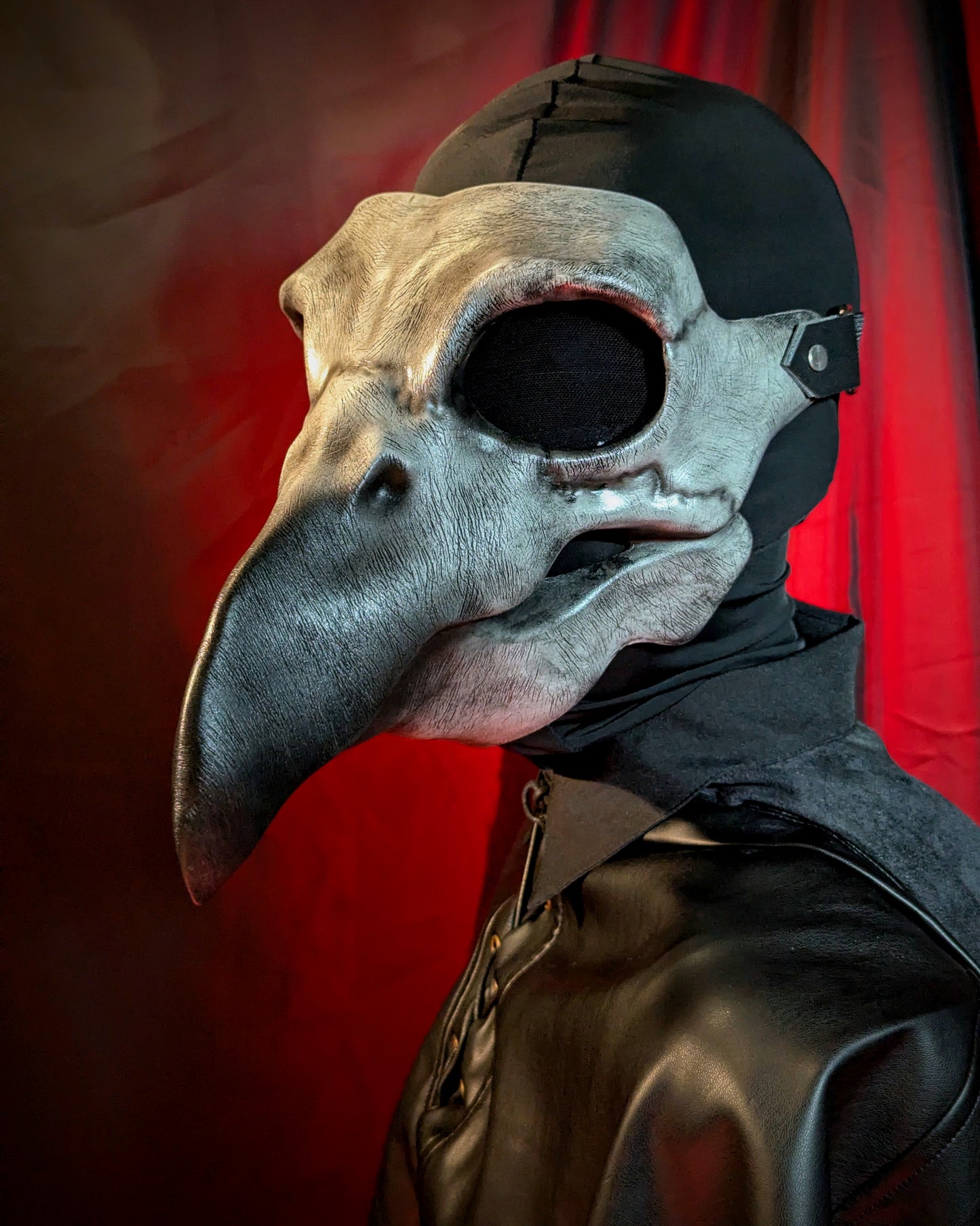 Person wearing a detailed bird-like plague doctor mask with a red curtain background