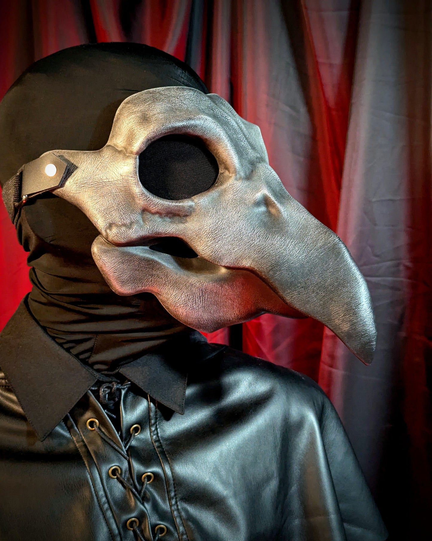 Person wearing a detailed bird-themed plague doctor mask against a red curtain background