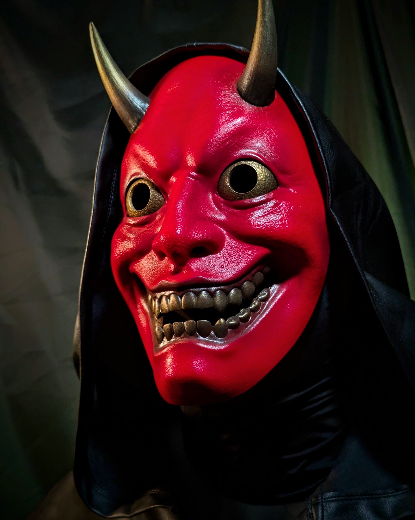 An upward facing angle of a person wearing a red hannya demon mask with a black hood.
