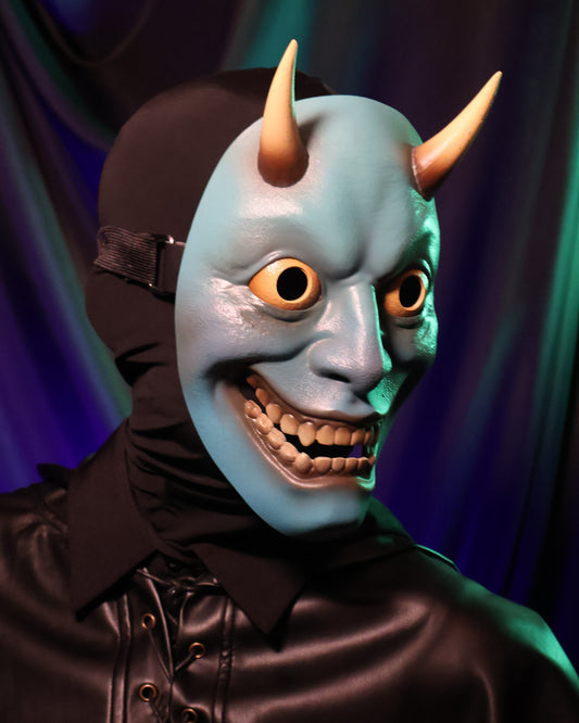 A quarter side angle of a person wearing a blue hannya mask with yellow horns, eyes, and teeth against a blue/green curtain background