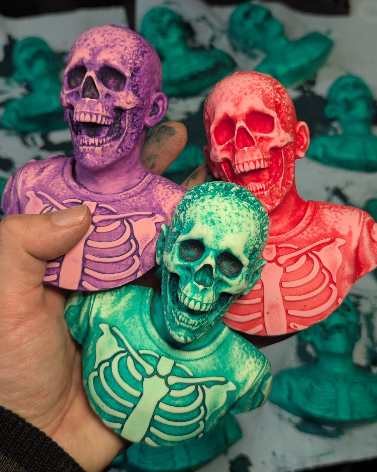 Colorful skeleton figurines held by a hand with a blurred workspace background