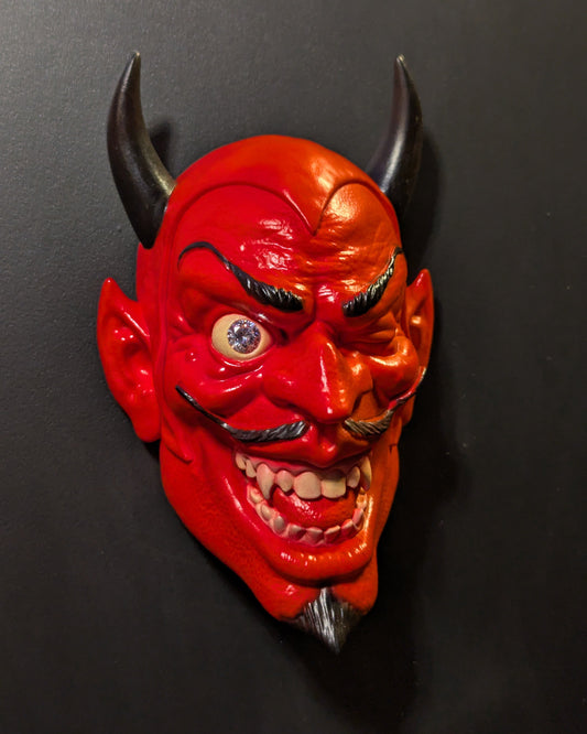 A red devil wall sculpture hanging from a black wall.