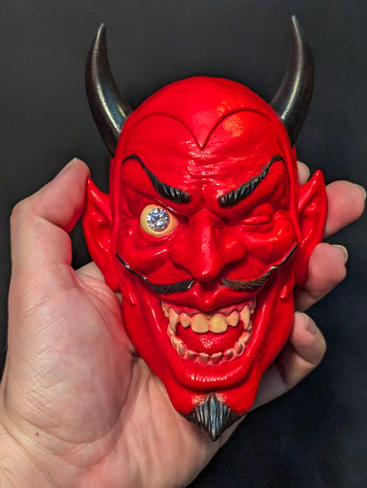 A red devil sculpture being held in a hand against a black background
