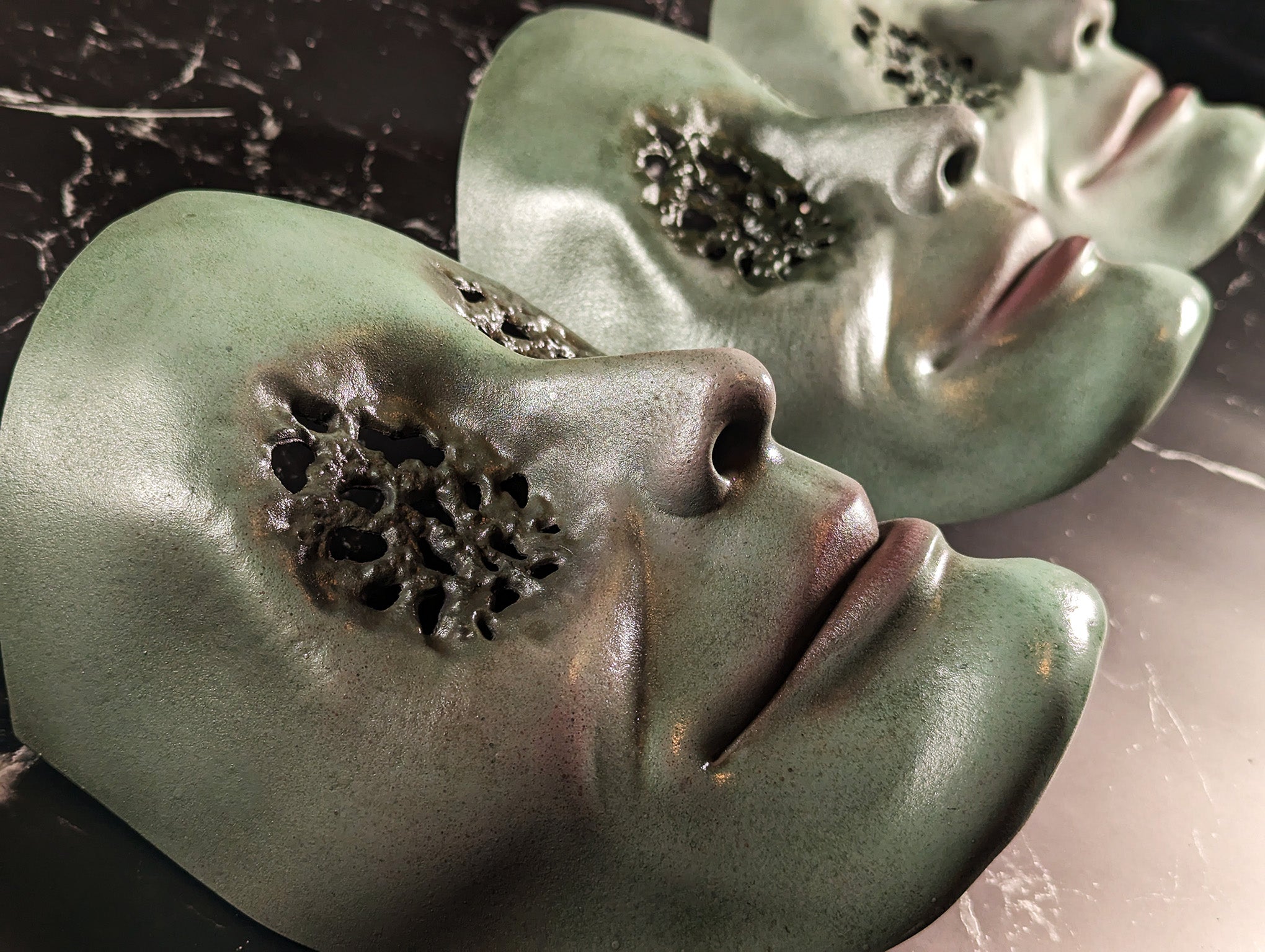 Three green masks with small holes for the eyes lined in a row on a black surface