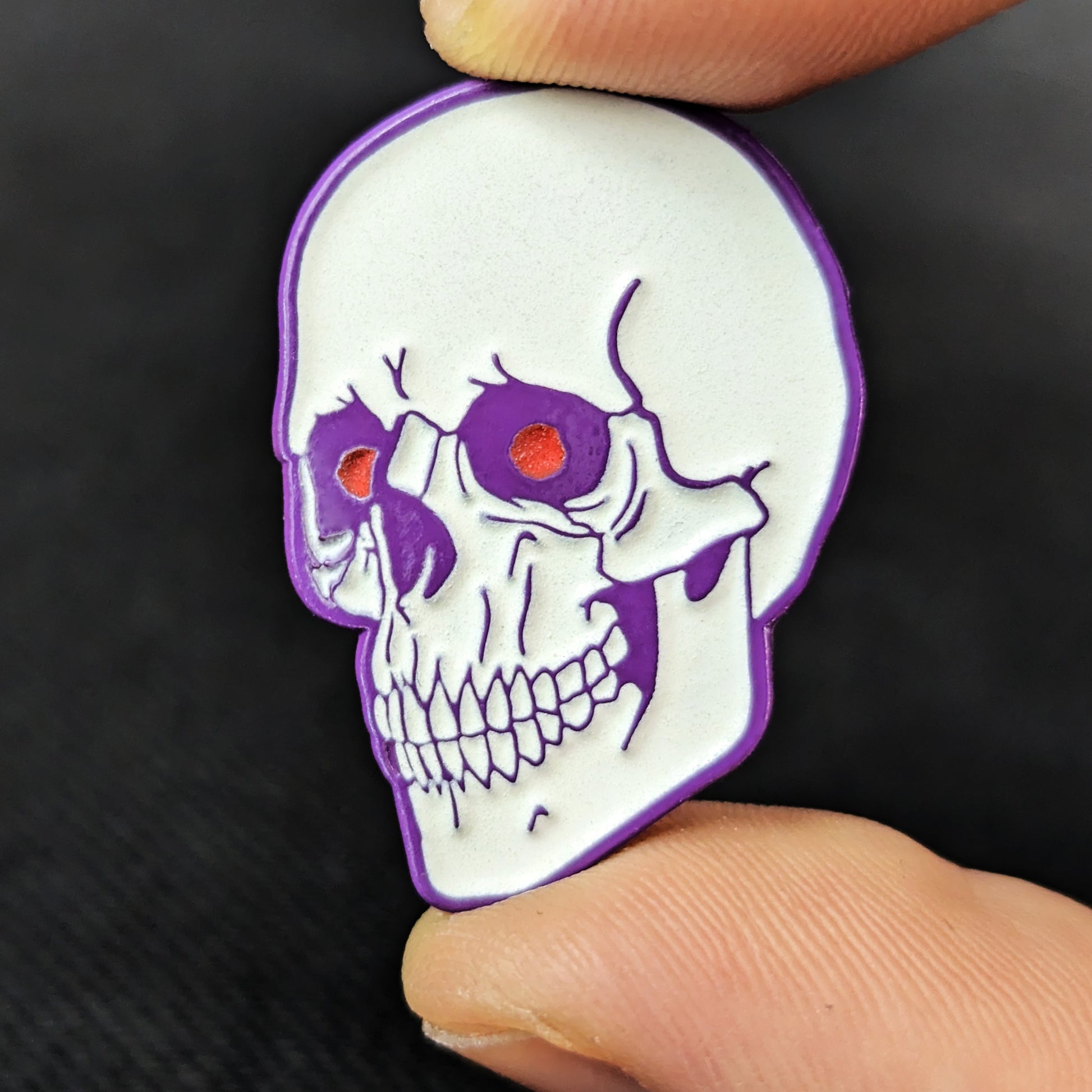 A white soft enamel human skull pin with purple plating and red eyes