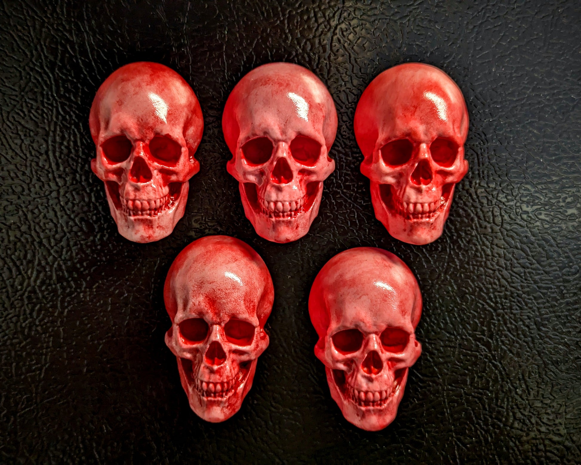 Five miniature pink skulls covered with a bright bloody red color