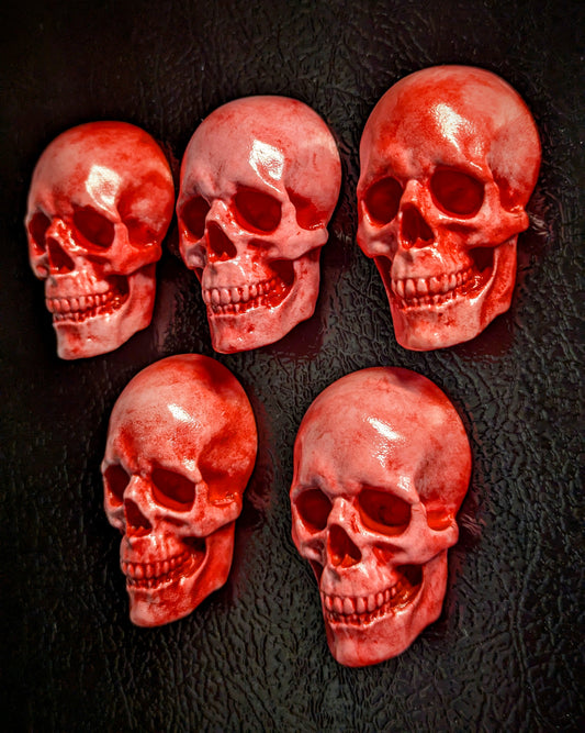 Five pink and red skull magnets on a black textured background