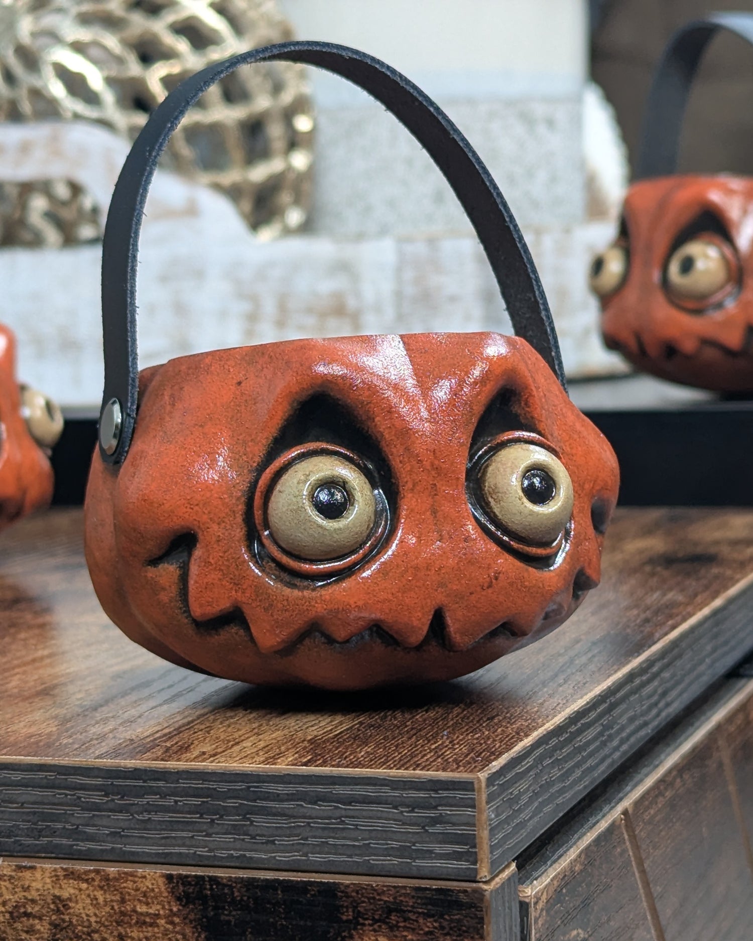 Decorative miniature pumpin with eyes, mouth, and leather handle on the corner of a wooden table