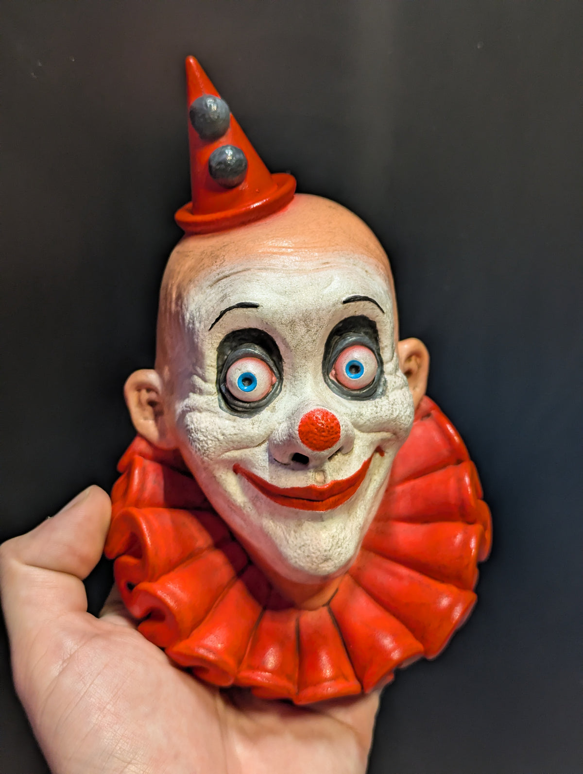 A clown sculpture with gray eye makeup and red clothing