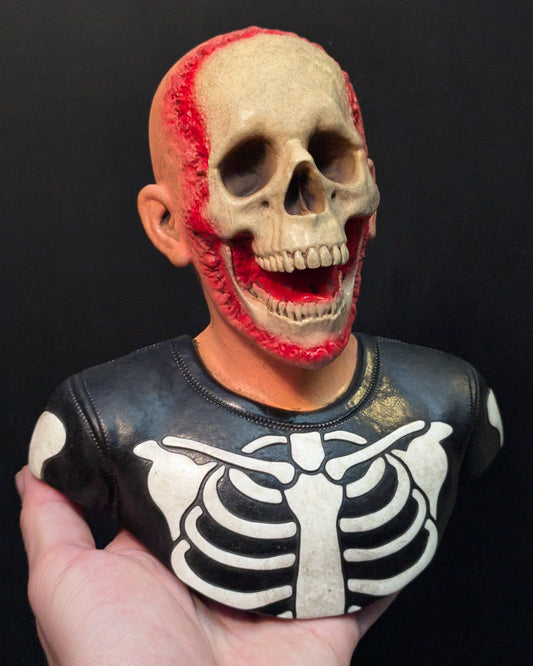 A resin sculpture of a skeleton trick or treater being held in one hand.