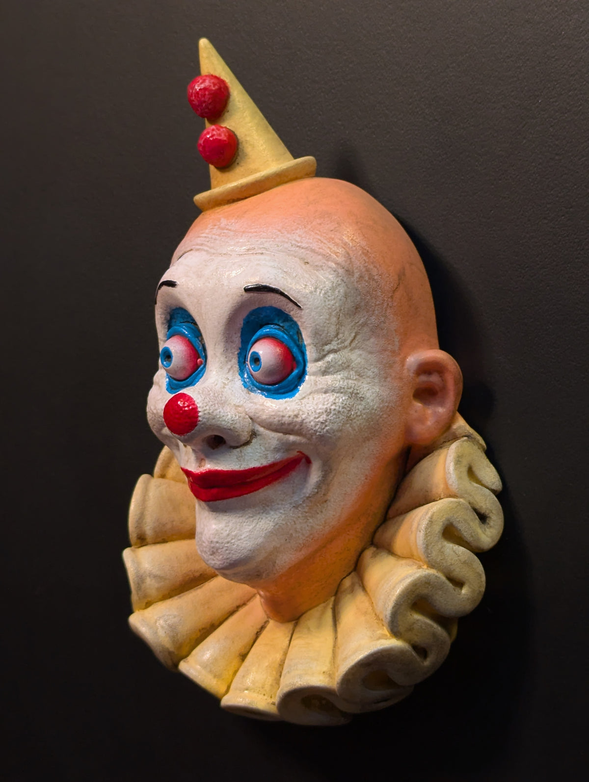 A resin clown sculpture mounted from a black wall