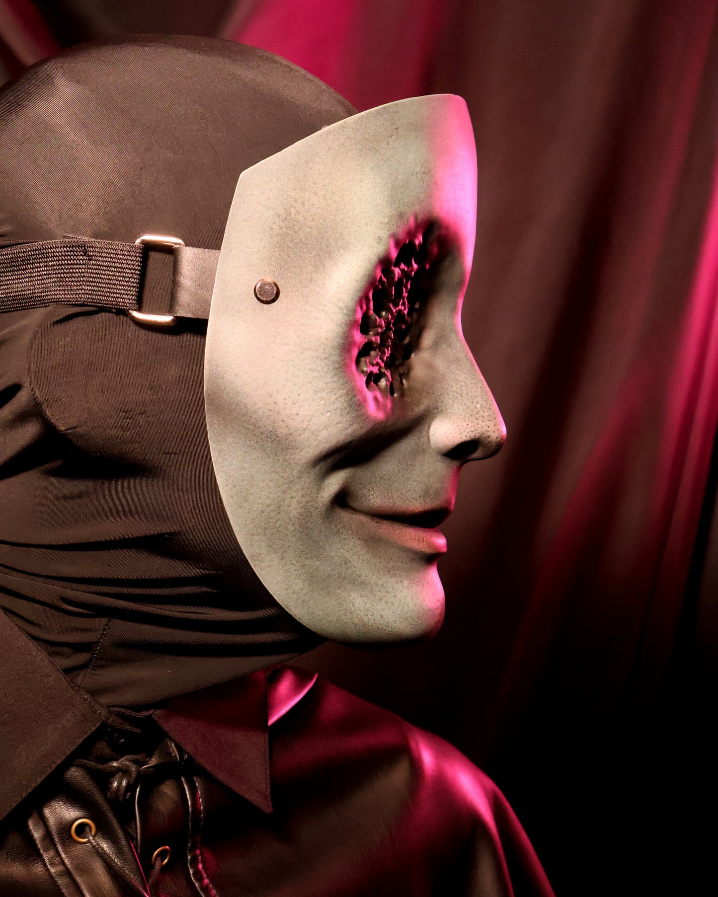 Side view of a person wearing a green mask with many small holes in the eyes on a dark background