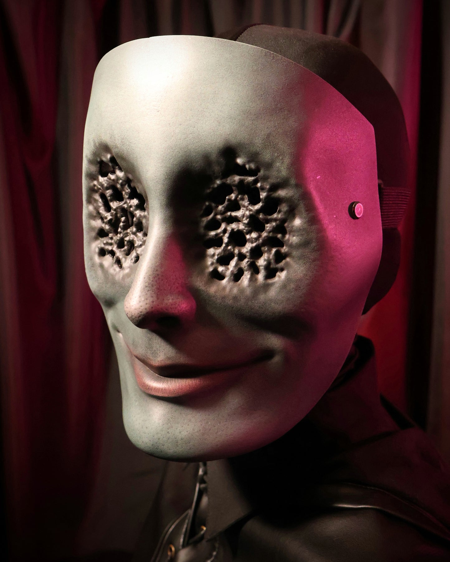 Quarter view of a person wearing a green mask with many small holes in the eyes on a dark background