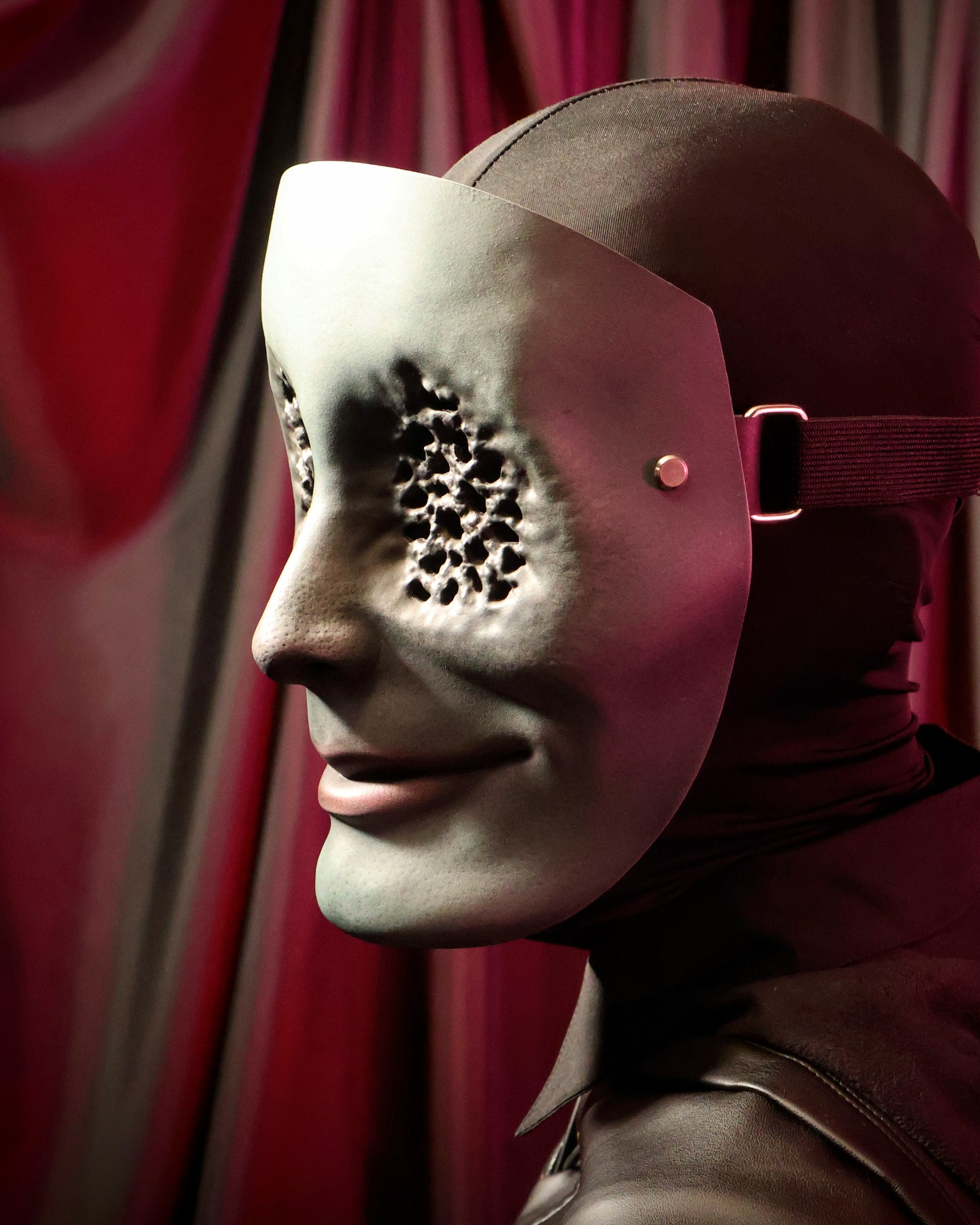 Side view of a person wearing a green mask with many small holes in the eyes on a dark background