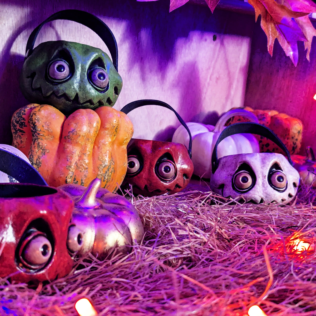 Several stylized miniature jack-o-lanterns are arranged on straw with purple and orange lights in  a fall themed background