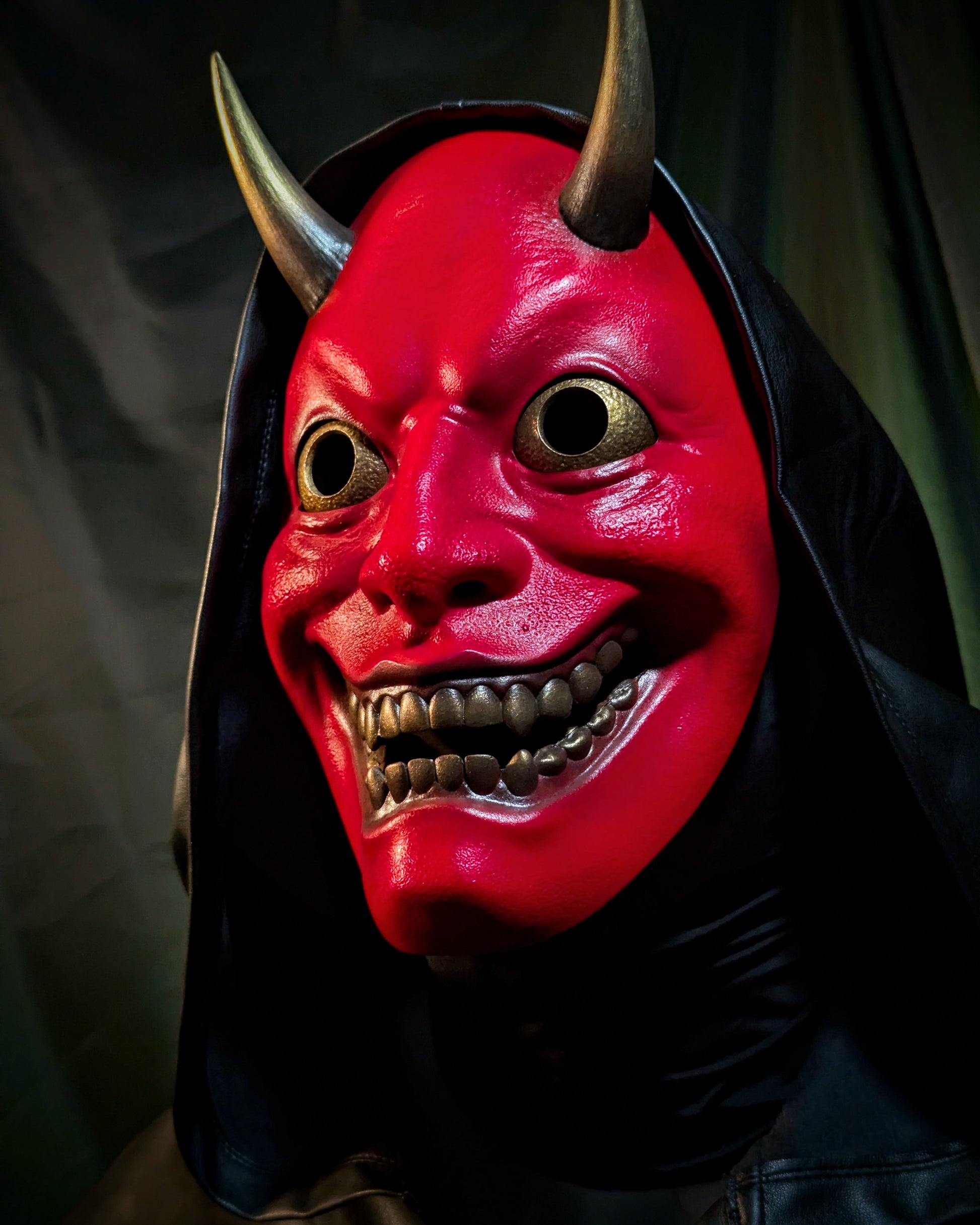 An upward facing angle of a person wearing a red hannya demon mask with a black hood.